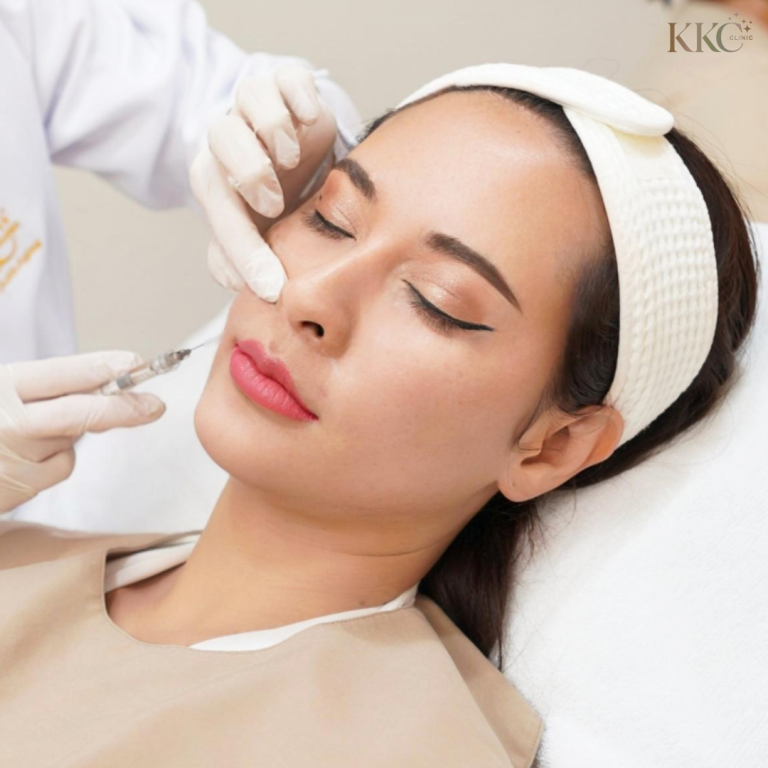 ผู้หญิงที่หลับตากำลังรับการฉีดฟิลเลอร์บริเวณร่องแก้มที่ KKC Clinic โดยผู้เชี่ยวชาญที่สวมถุงมือ