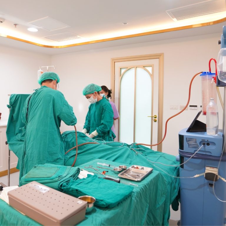 Doctors performing a VASER liposuction procedure in an operating room at KKC Clinic. Surgical equipment and suction machines are visible in the room.