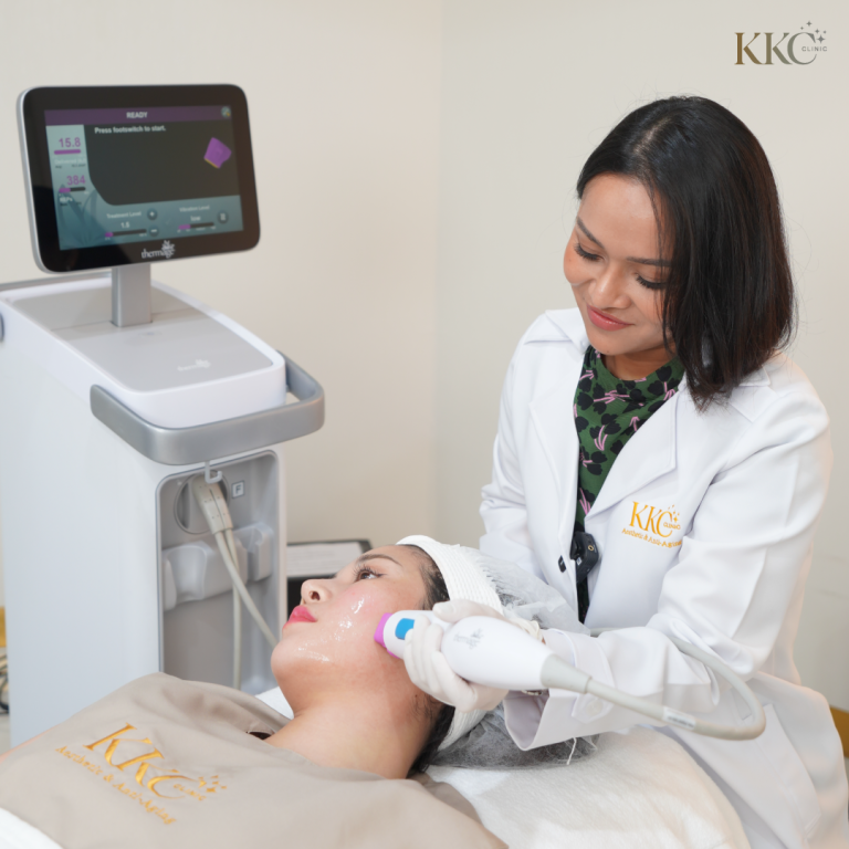 คุณหมอที่ KKC Clinic ในชุดกาวน์สีขาวกำลังทำทรีตเมนต์ Thermage บนใบหน้าของคนไข้ด้วยหัวทรีตเมนต์ พร้อมเครื่อง Thermage ที่กำลังทำงานอยู่