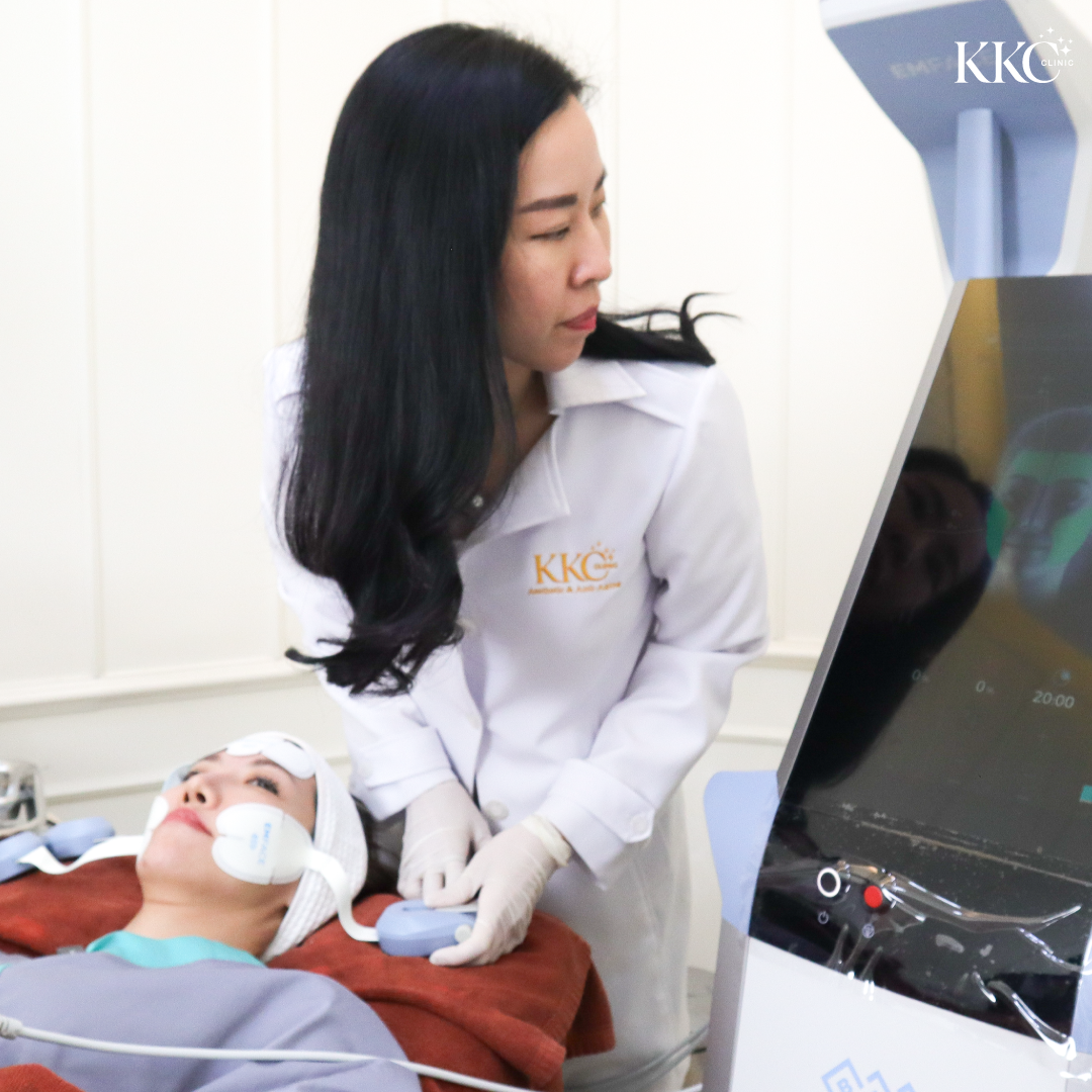 แพทย์ที่ KKC Clinic กำลังทำการรักษา EMFACE ให้กับคนไข้ที่นอนอยู่ โดยมีแผ่นติดอยู่บนใบหน้าและเครื่องมือการรักษาอยู่ในภาพ