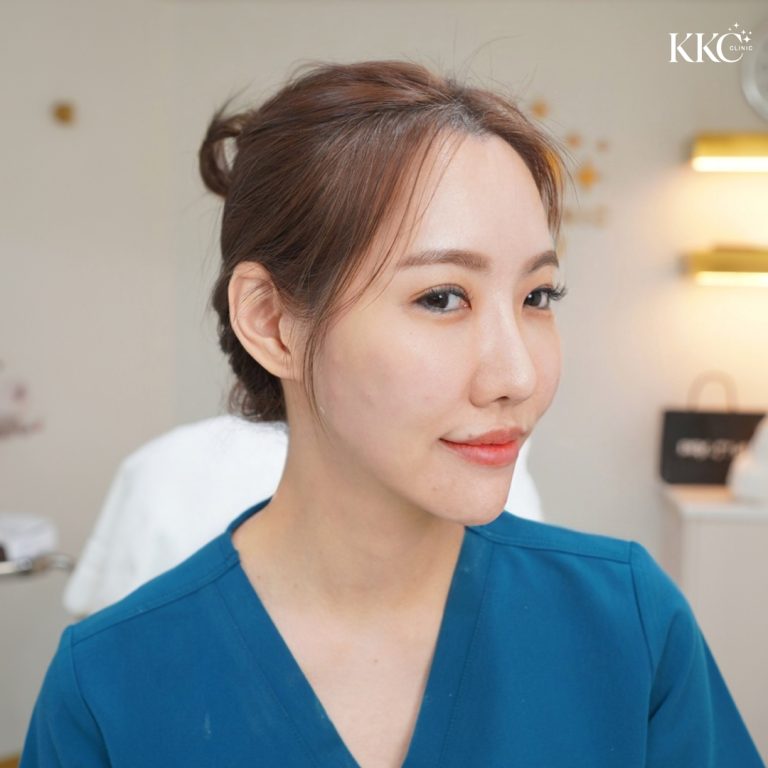 พญ.วรวรรณ เตชะสมบูรณ์ ในชุดเครื่องแบบทางการแพทย์สีฟ้า หลังรับการรักษาด้วย Profhilo นั่งอยู่ในห้องทำหัตถการที่มีบรรยากาศเงียบสงบและมืออาชีพ