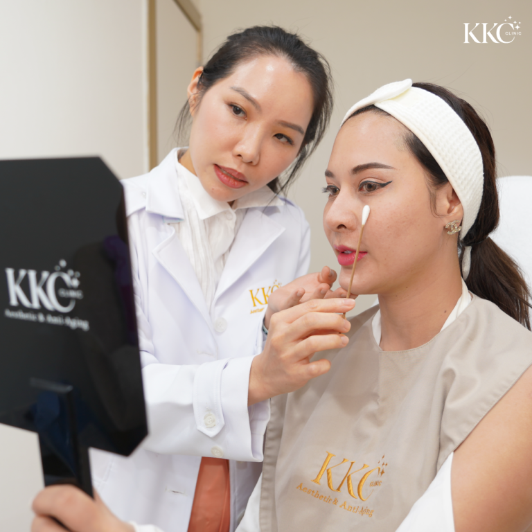 แพทย์ประจำ KKC Clinic ในชุดกาวน์สีขาว กำลังให้คำปรึกษาผู้ป่วยที่ถือกระจก และใช้สำลีแท่งแตะบนใบหน้าเพื่อวางแผนการฉีดโบท็อกซ์