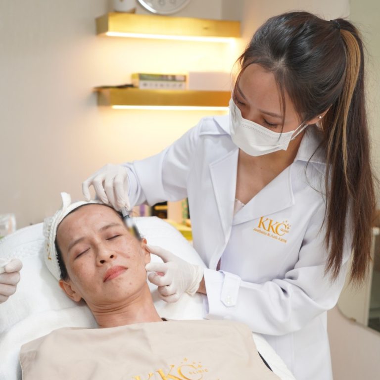 A doctor wearing a white coat with the KKC Clinic logo and a mask performing a thread lift procedure on a patient's face while the patient lies on a treatment chair.