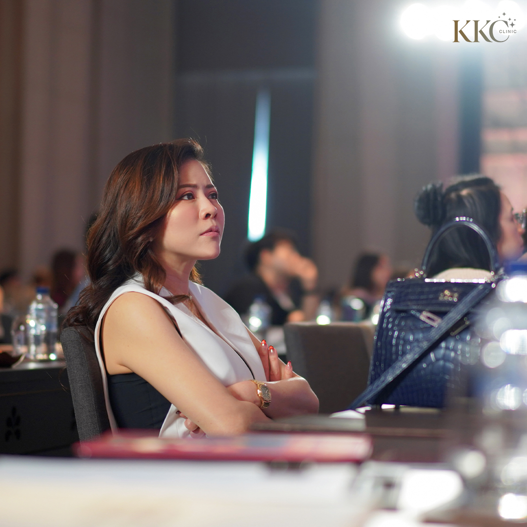 พญ.ของขวัญ ฟูจิตนิรันดร์ นั่งกอดอกฟังการบรรยายอย่างตั้งใจในงานสัมมนา MD Codes บรรยากาศมีแสงนุ่มนวลในพื้นหลัง