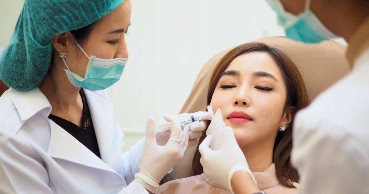 Doctor performing meso fat dissolving injections on a female patient's lower face while assistants support the procedure.