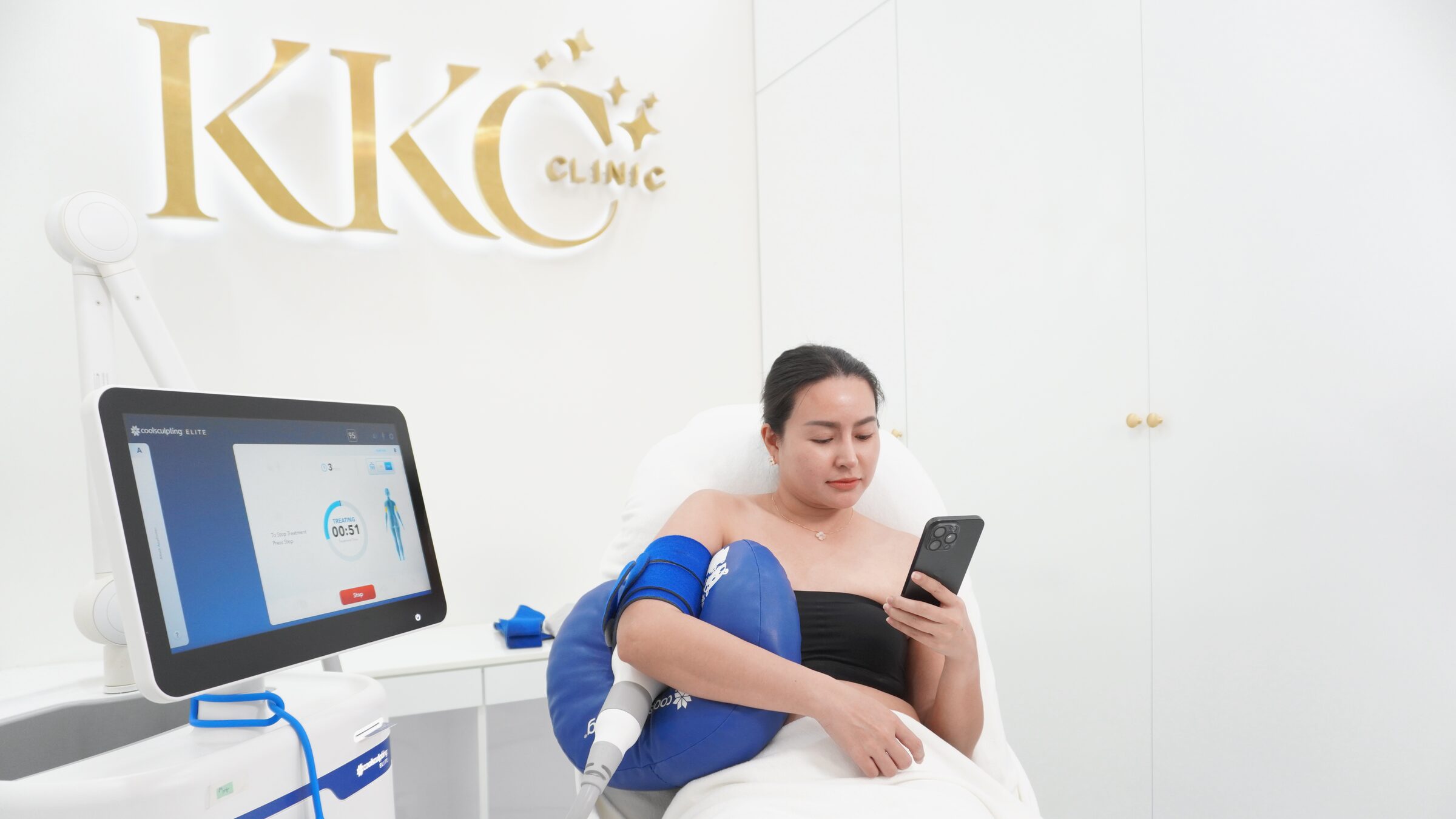A client reads her phone during a CoolSculpting Elite session on her upper arm