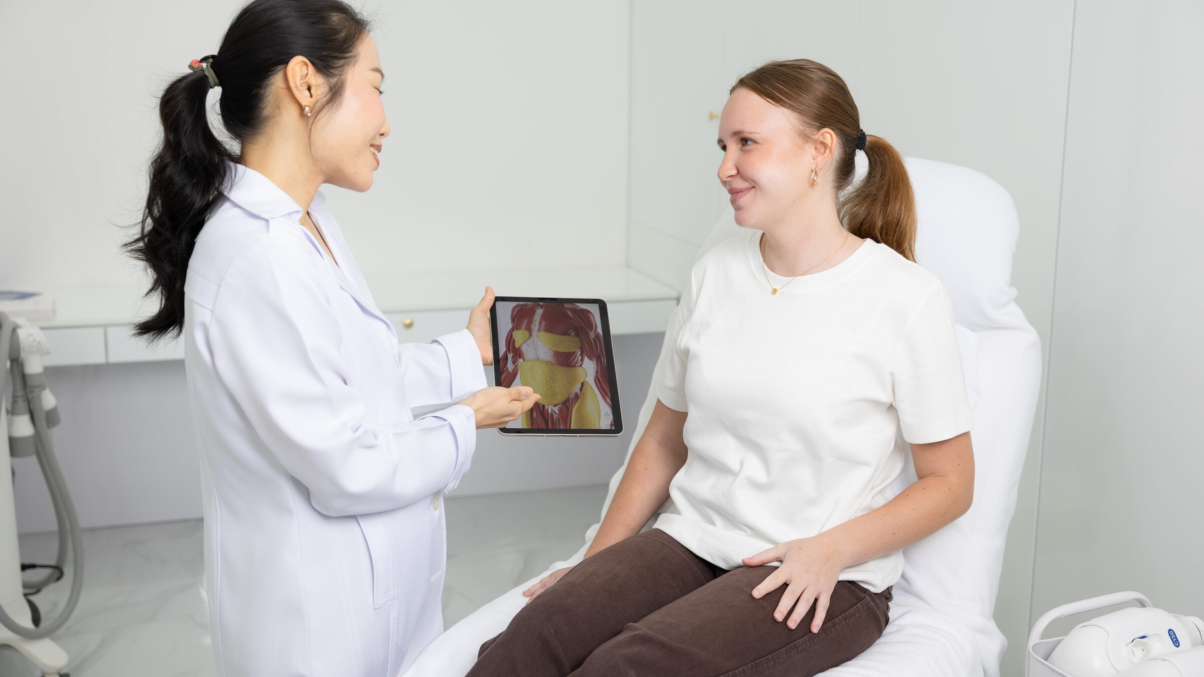 Dr. Monthinee Techasomboon (Dr. Pom) explains CoolSculpting to a client using an anatomy image on a tablet